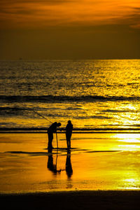 Silhouette people on beach against sky during sunset