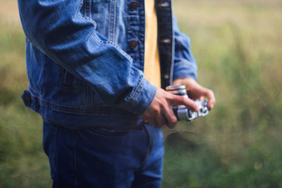 Male hands holding retro photo camera on green nature background. film grain effect. man in jeans 