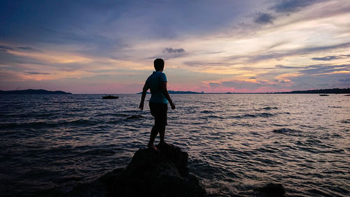 Full length of man standing on rock at beach during sunset