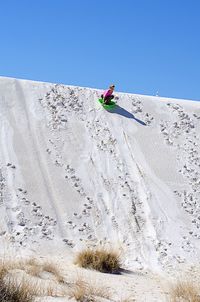 Low angle view of boy with sled on snowcapped mountain against clear sky