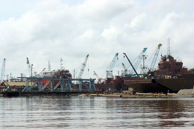 Cranes at harbor against sky