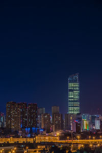 Illuminated buildings in city against clear sky at night