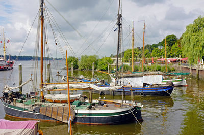 Sailboats moored in river against cloudy sky