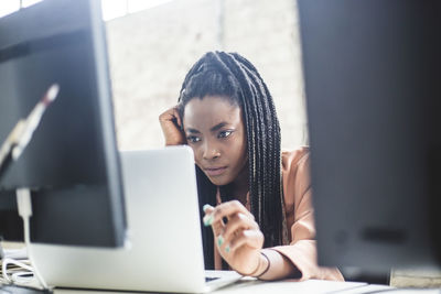 Serious female it expert concentrating on computer codes while using laptop at workplace
