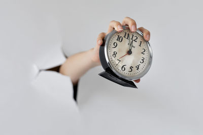 Close-up of woman hand holding clock against white background