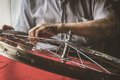 Midsection of mechanic repairing bicycle wheel at workshop