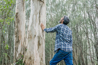 Man standing by tree trunk in forest