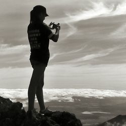 Woman photographing landscape against sky