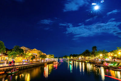 Illuminated city by river against sky at night