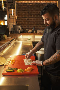 Side view of male cook in gloves and uniform preparing appetizing sushi rolls at table in asian restaurant