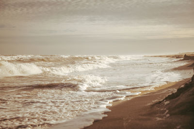 Waves rushing towards shore against sky