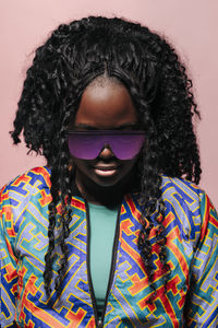 Portrait of african american woman with curly hair and bright colorful clothes and modern sunglasses on pink background