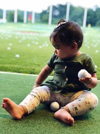 Cute baby girl playing with golf balls while sitting on grassy field