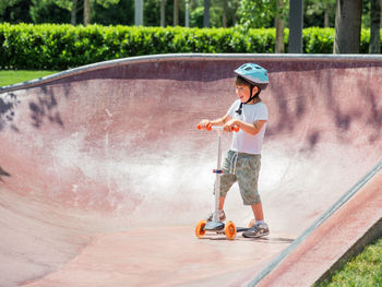 Boy rides kick scooter in skate park. concrete bowl structures in urban park. training to skate.