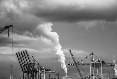 Cranes against factories emitting smoke