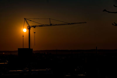 Silhouette cranes at construction site during sunset