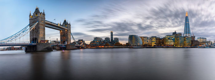 Panoramic view of tower bridge and illuminated buildings by thames river at dusk