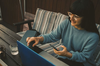 Smiling woman using laptop and mobile phone on table in holiday villa