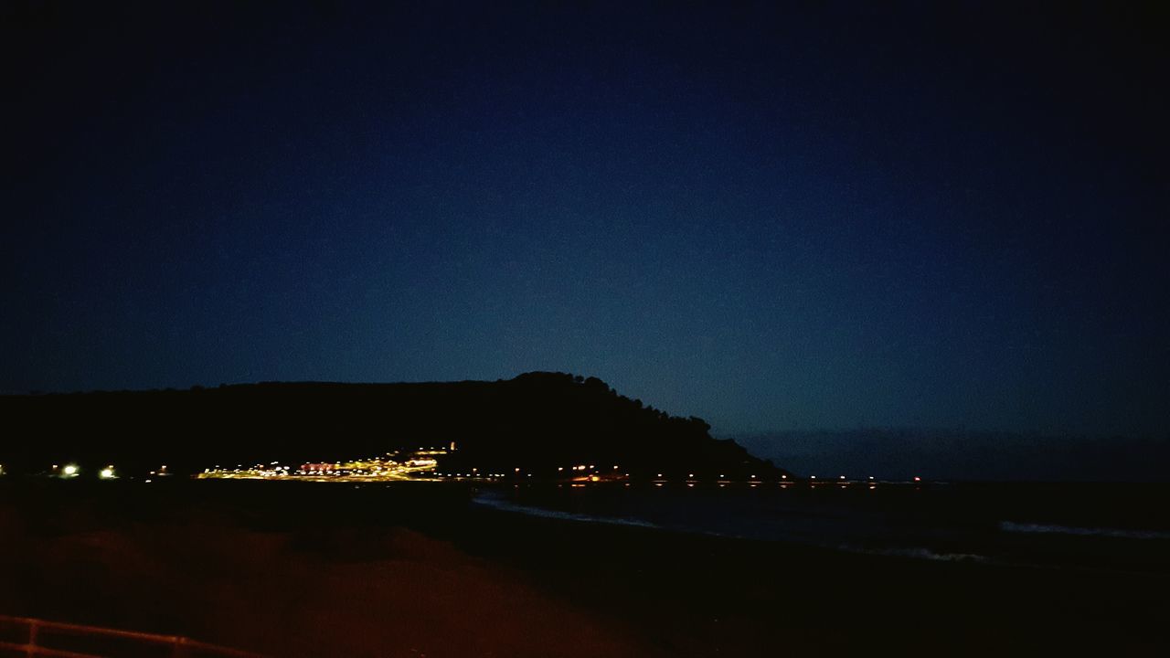 night, illuminated, copy space, water, sky, built structure, clear sky, architecture, dark, sea, beach, building exterior, river, transportation, road, dusk, tranquility, outdoors, street light, city