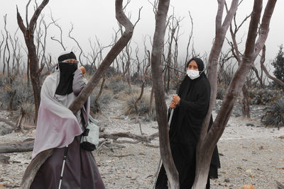 Women wearing mask standing by bare trees in forest