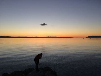 Silhouette man standing on beach against clear sky during sunset