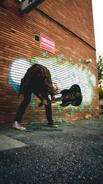 Side view of woman standing against graffiti wall