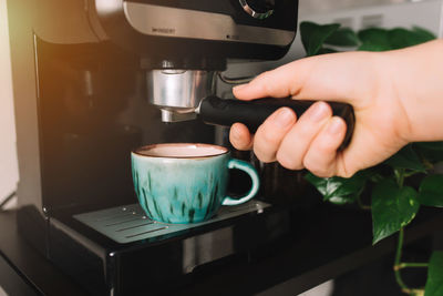 Hand holding portafilter, green cup of coffee at coffee maker machine, coffee time