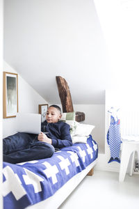 Teenage boy using laptop while lying on bed at home