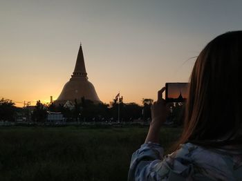 Rear view of woman photographing against sky at sunset