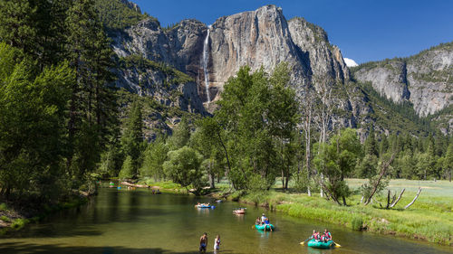 People on lake by mountain against sky