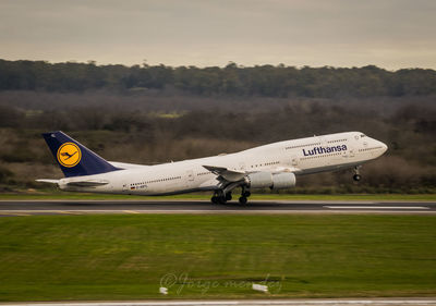 Airplane flying over airport runway against sky