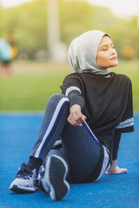 Thoughtful female athlete stretching at stadium