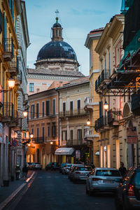 Illuminated buildings by street in city against sky