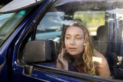 Woman touching cheek while looking in side-view mirror of car