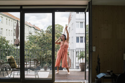 Carefree woman listening to music while dancing in balcony