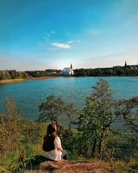 Rear view of woman sitting on riverbank against sky