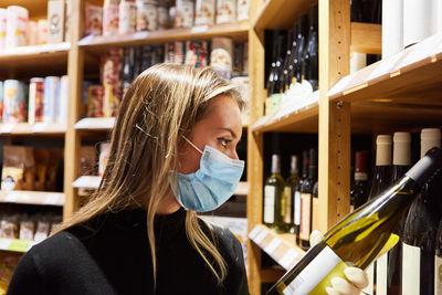 Side view of woman wearing mask holding wine bottle