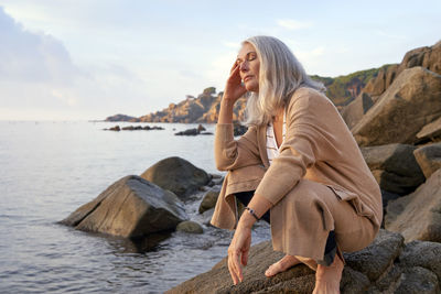 Gray haired woman with eyes closed on rock