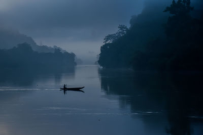 Silhouette of man on boat in lake against sky