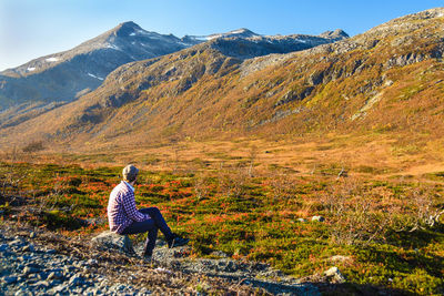 Rear view of woman sitting on mountain against sky