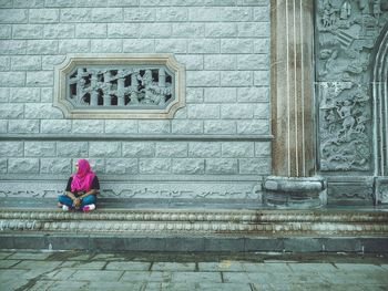 Woman looking away sitting against built structure