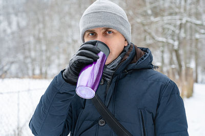 A man drinks from a purple thermos on a winter walk