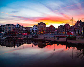 Buildings by river against sky at sunset