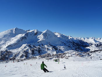 People skiing on snowcapped mountain against clear blue sky