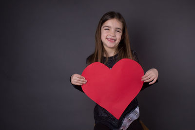 Portrait of smiling young woman holding heart shape against black background