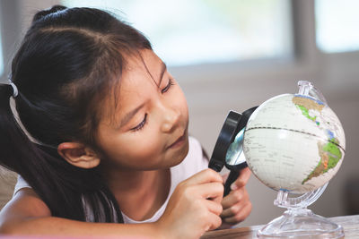 Girl looking at globe through magnifying glass in classroom