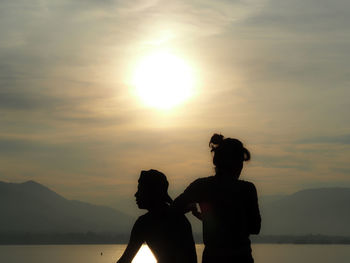 Silhouette people on shore against sky during sunset