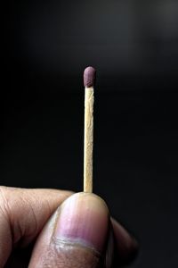 Cropped hand holding matchstick against black background