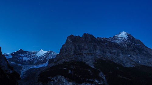 Low angle view of snowcapped mountains against clear blue sky