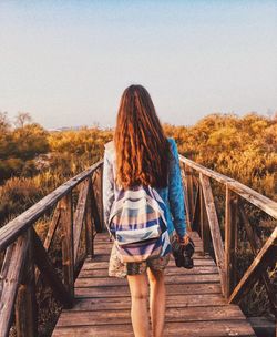 Rear view of woman on footbridge against sky